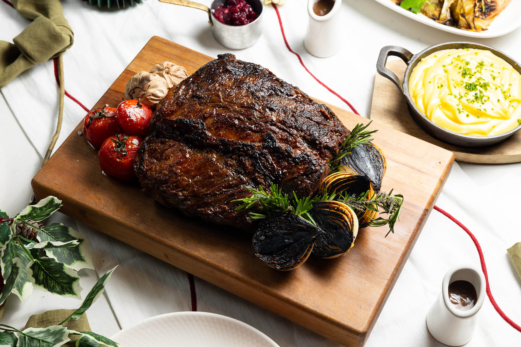 Aged beef scotch fillet carved on a wooden board with rosemary and charred onion.