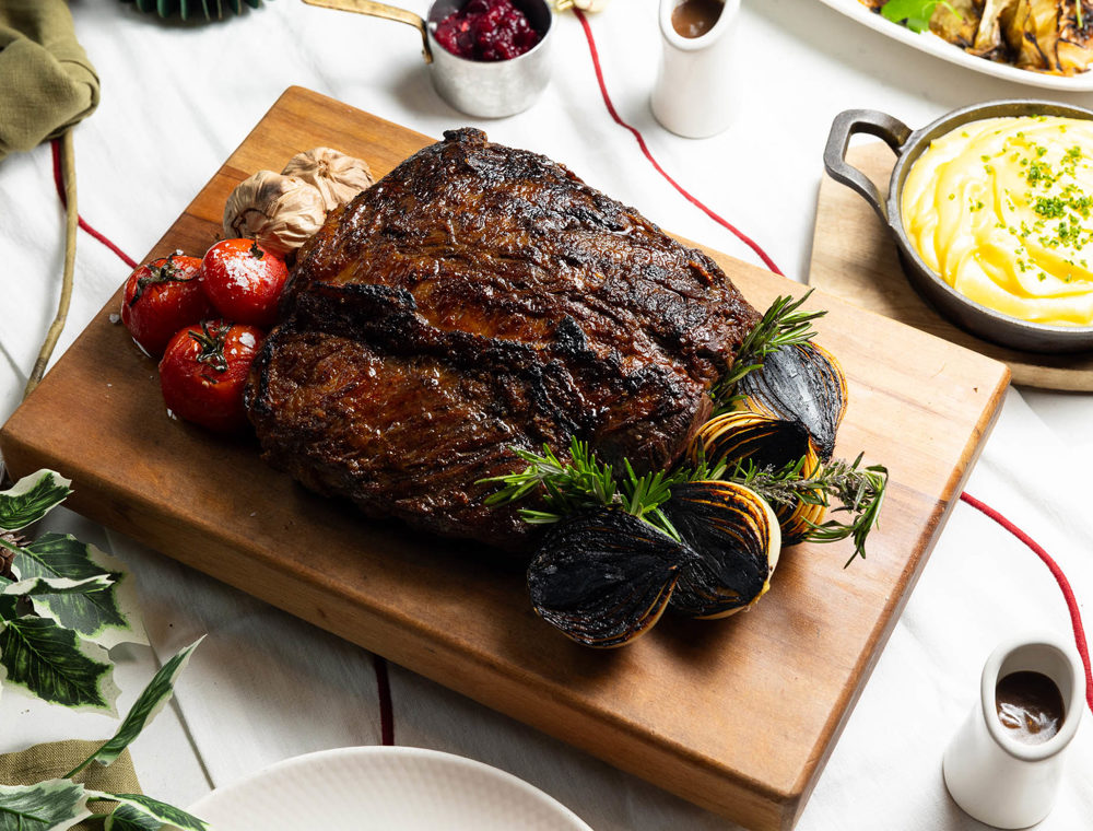 Aged beef scotch fillet carved on a wooden board with rosemary and charred onion.