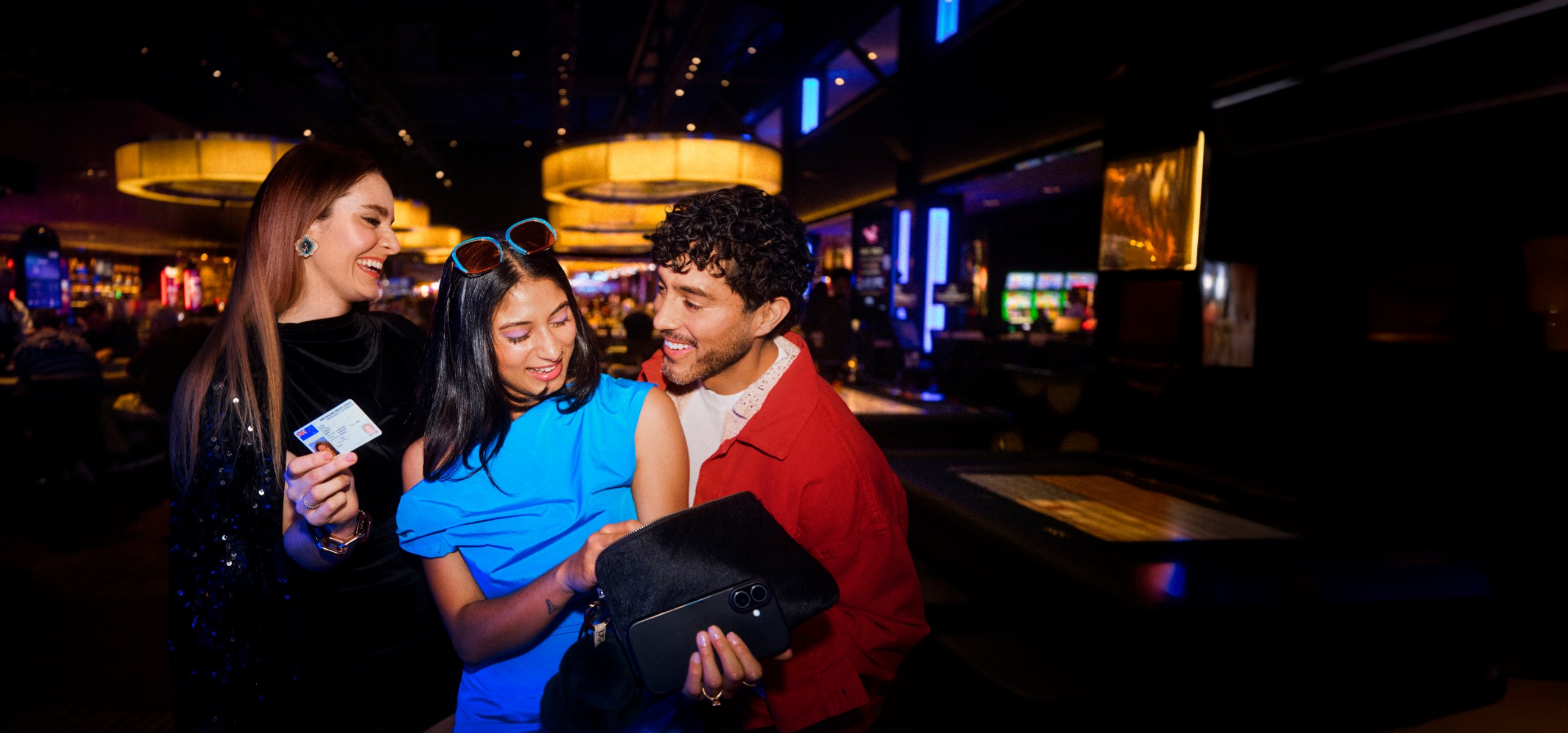 Three friends laughing together on the SkyCity Auckland casino floor, one holding up her ID