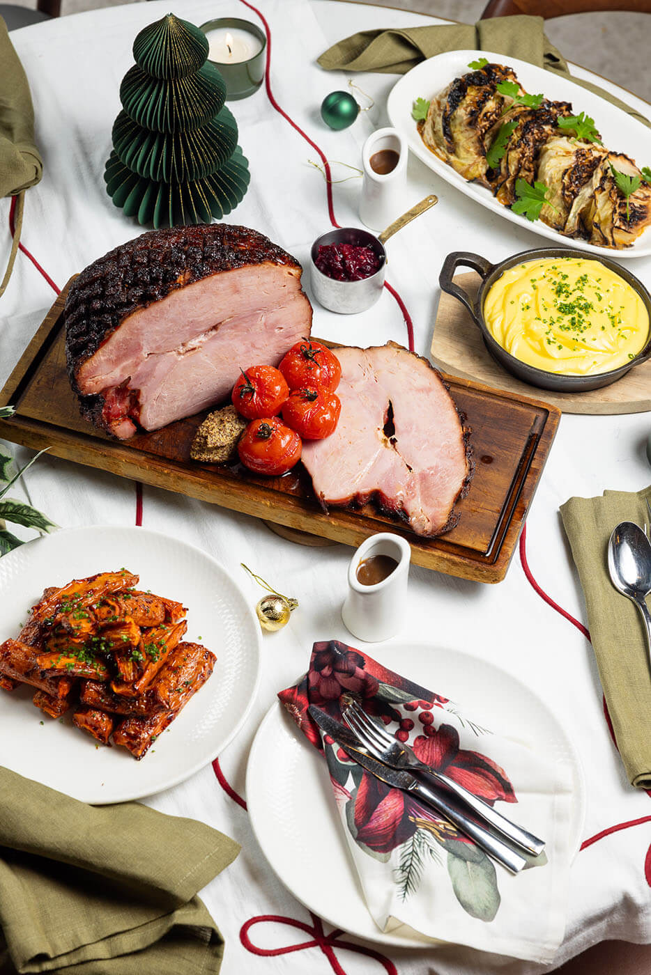 Maple glazed ham carved on a wooden board with roasted tomatoes and mashed potato.