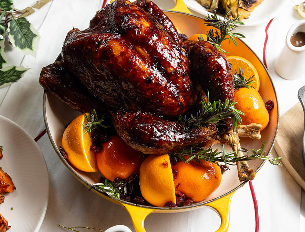Whole roast turkey glazed and served in a casserole dish with oranges and rosemary.