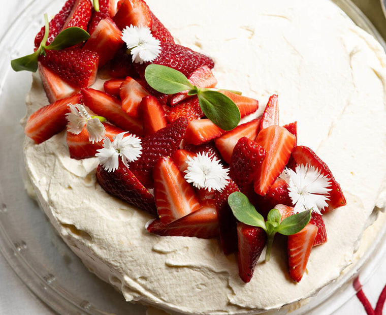Strawberry pavlova topped with cream, fresh strawberries and edible flowers.